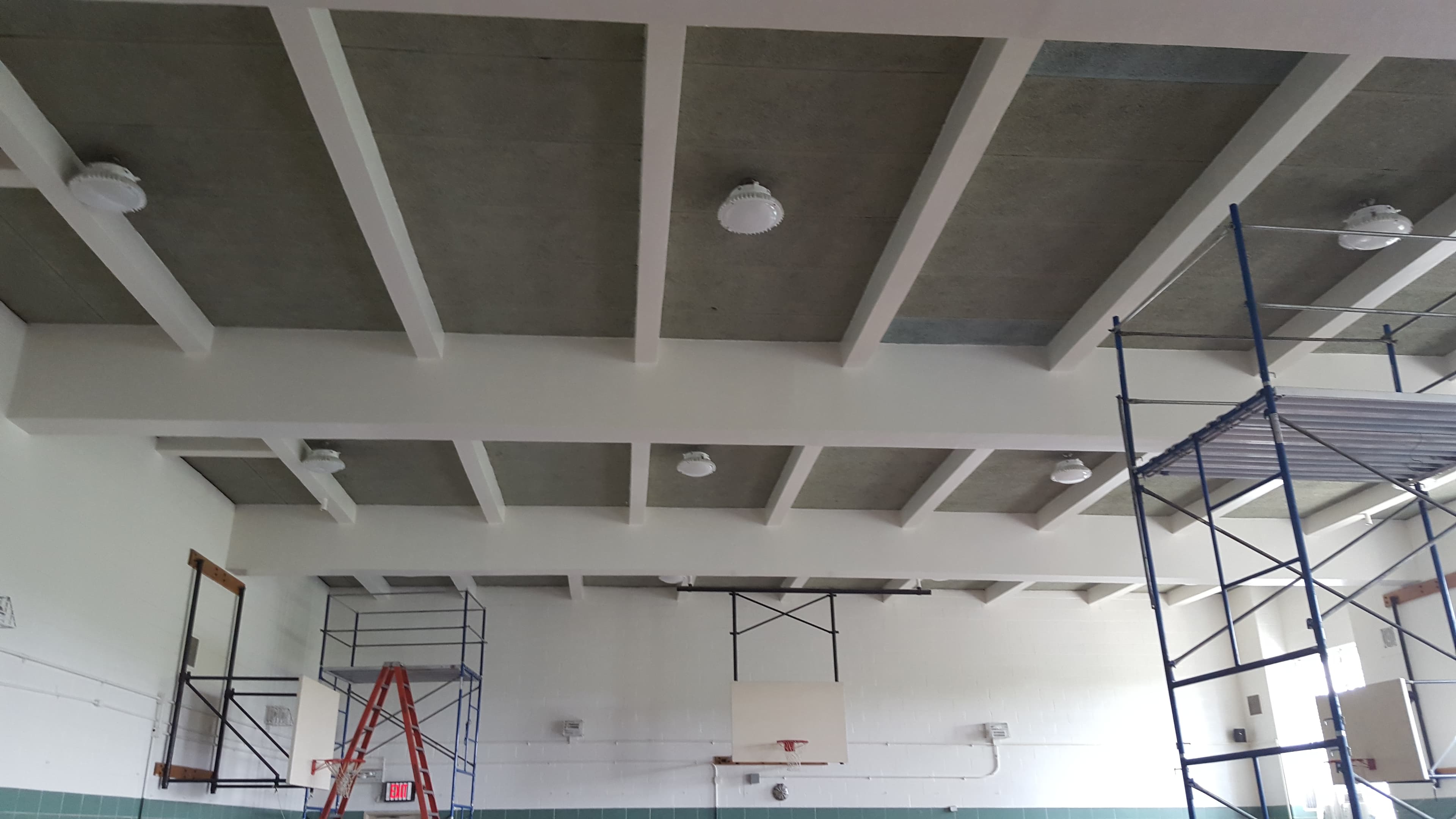 Various scaffolds and ladders in a gymnasium, showing 6 mounted light fixtures