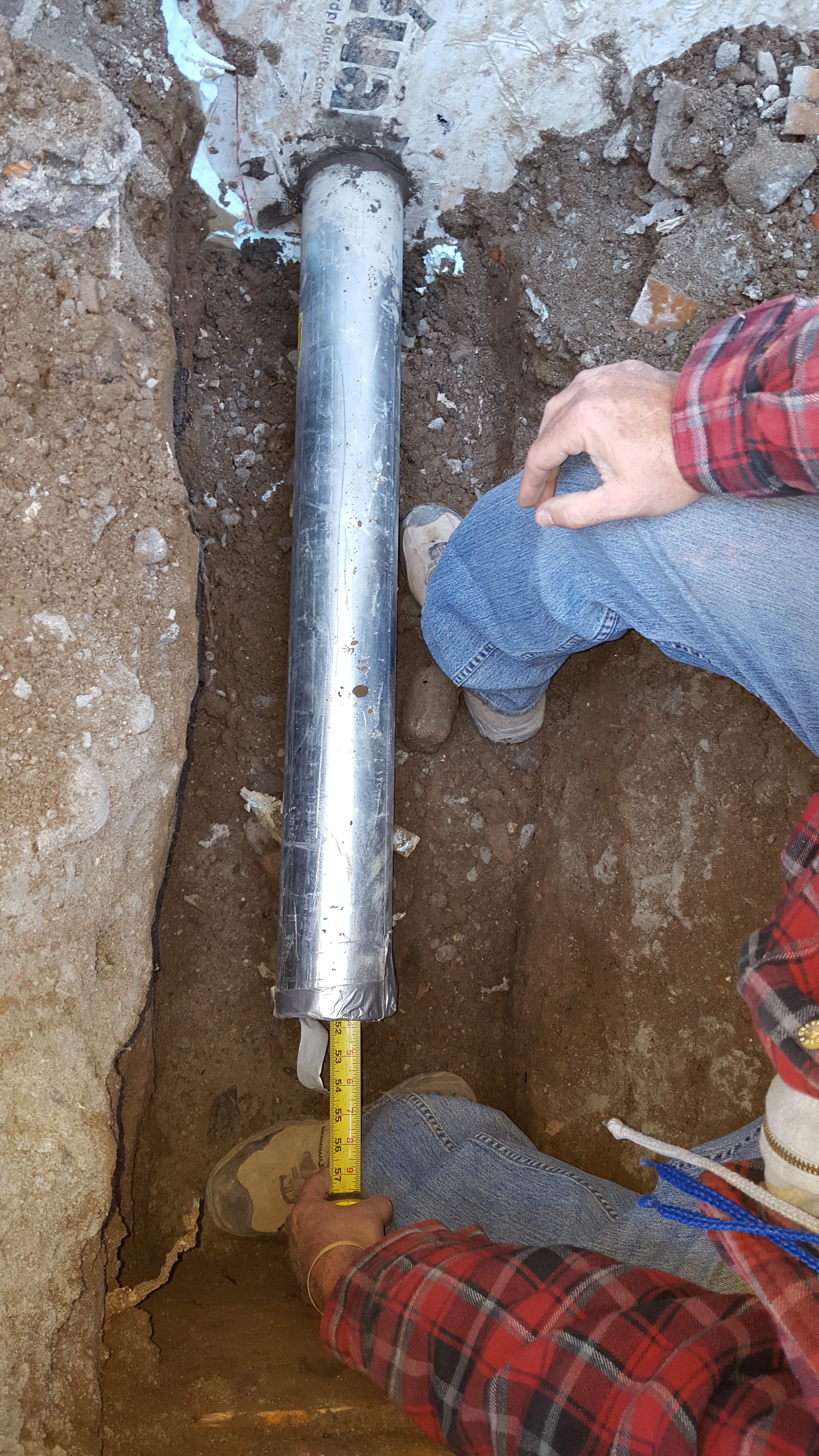 A trench that was dug to install pipe, with tape measure coming out through the pipe from inside the building